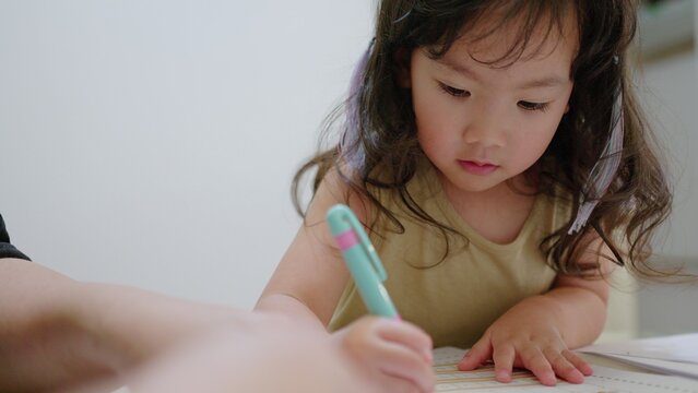 A young Asian toddler concentrates on her drawing activity at home, developing fine motor skills and learning as part of her early childhood education.