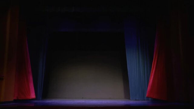 Panning shot of red stage curtains parting to reveal empty theater stage with dim spotlight and dark backdrop, gradual slow motion reveal