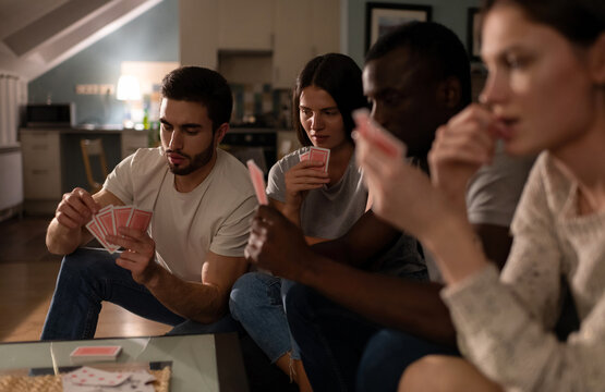 Serious guy playing card during game with diverse friends at home