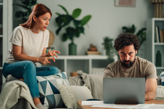 Woman arguing with man glued to laptop, showing relationship problems, technology addiction, and communication breakdown