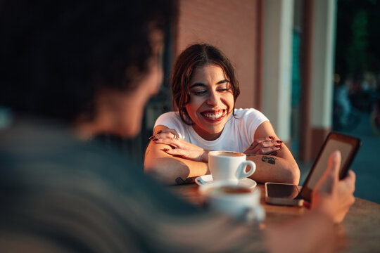 Happy young woman laughing with friend, enjoying coffee and conversation at an outdoor cafe