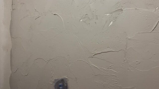 The process shows a person applying plaster onto a wall in a small room. The focus is on the steps taken to cover the wall smoothly and evenly.