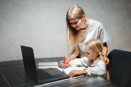Mother helping her child girl writing and study in online school using laptop at home, homeschooling and digital education kid learning with modern technology family bonding candid moments