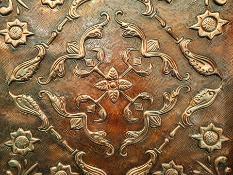 Texture of ancient copper metal carving relief with sunflower motifs and traditional vines forming a symmetrical pattern on the surface of a decorative handicraft plate.