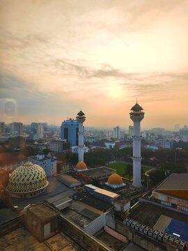 Bandung City, Indonesia - July 08, 2026: Urban landscape view with twin minarets of the Bandung Grand Mosque against a yellowish sunset sky backdrop.