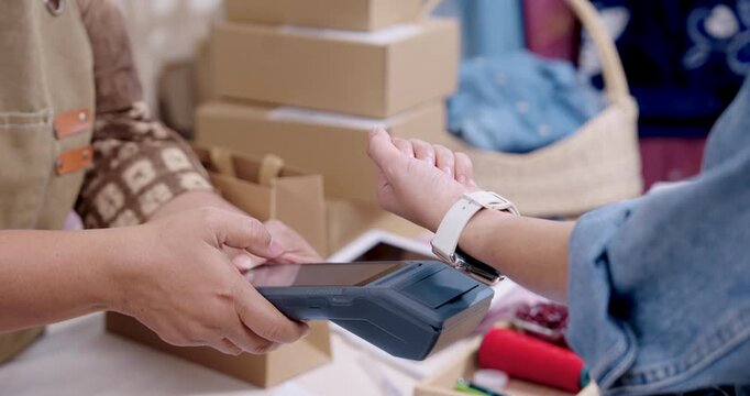 Asian family business owner completes cashless payment on POS terminal, senior woman entrepreneur confirms order checking, prepares wholesale parcel box, continues online shop packaging workflow.