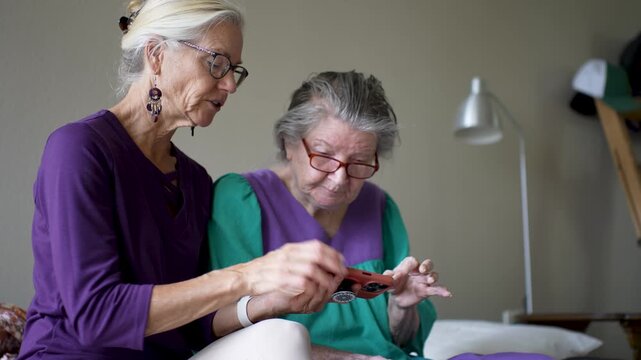 Mature daughter visits her elderly mother at a senior care facility. They talk and share photos while enjoying time together.