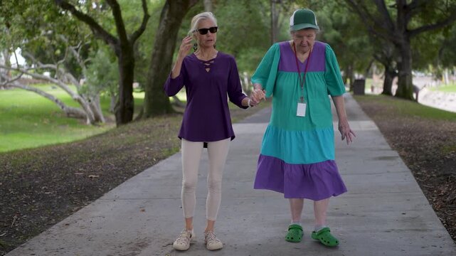 Elderly mother and mature daughter walk together in a park, sharing stories and enjoying their time together outside.