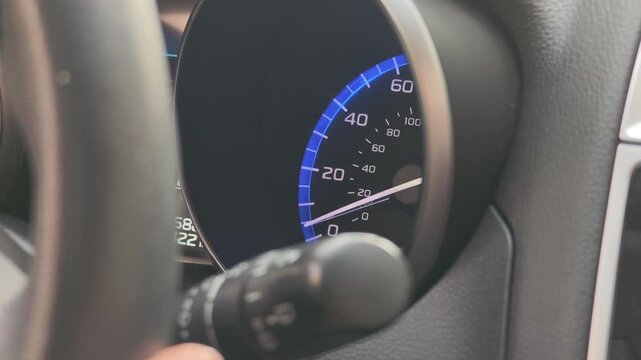 Close up view of a modern car dashboard showing the speedometer needle moving up. The vehicle is accelerating from a complete stop