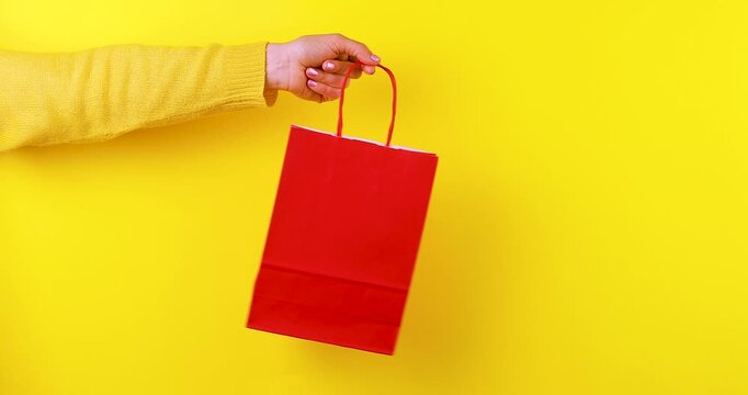 Close-up video of a hand holding and rotating a red paper shopping bag on a bright yellow background. Retail and shopping concept for stores, gifts, sales, branding, packaging, and e-commerce.