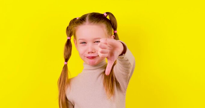Video of a smiling young girl on a yellow background giving a thumbs up, then changing to a thumbs down while her expression shifts to a playful smirk. Concept of approval, rejection, opinions, and