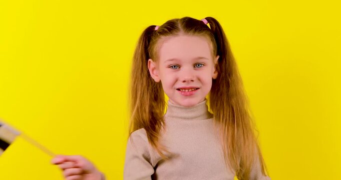 Video of a young girl waving a black and white checkered racing flag on a yellow background. Concept of race start, finish line, victory, competition, motorsport, and celebration.