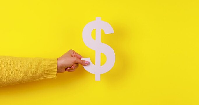 Close-up video of a 3D dollar symbol appearing in a hand on a bright yellow background. Concept of money, finance, wealth, investment, profit, income, savings, business, and financial success.