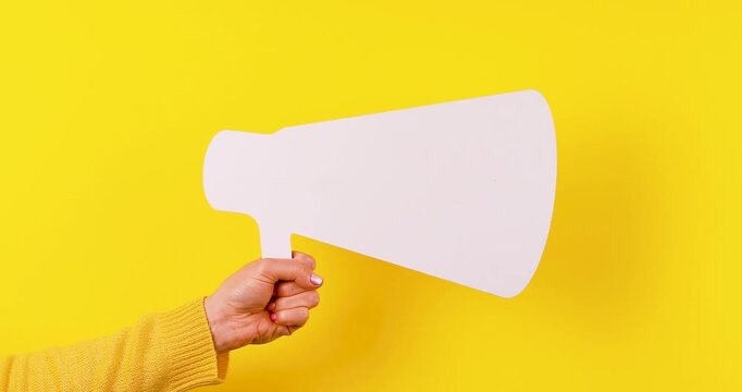 Close-up video of a hand holding a 3D megaphone symbol on a bright yellow background. Concept of announcements, marketing, promotion, advertising, public communication, and brand awareness.