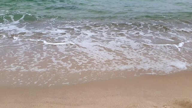 Close-up of stormy water surface with clean turquoise coastal surf waves rolling on empty sandy beach and foam patterns on wet sand on Baltic sea shore. Tranquil seashore aquatic natural background.