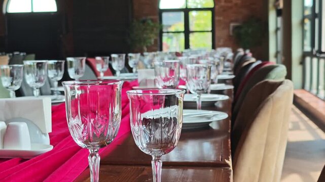 Beautifully served long wooden table ready for a celebration in a restaurant. Crystal glasses and white plates set for a festive dinner