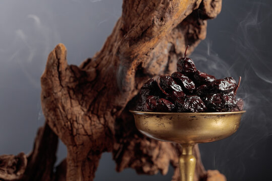 Dry cured black olives in a vintage brass bowl on a background of weathered olive tree snags.