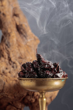 Dry cured black olives in a vintage brass bowl on a background of weathered olive tree snags.