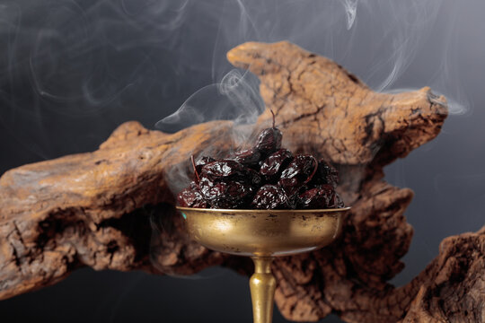 Dry cured black olives in a vintage brass bowl on a background of weathered olive tree snags.