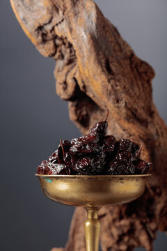 Spicy dried black olives in a vintage brass bowl on a background of weathered olive tree snags.