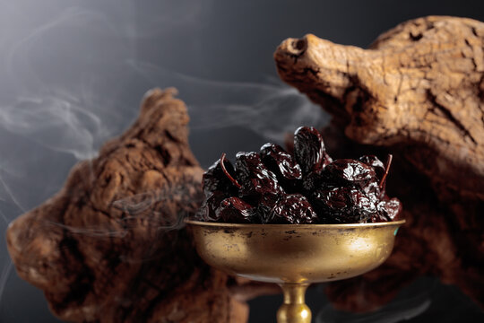 Dry cured black olives in a vintage brass bowl on a background of weathered olive tree snags.