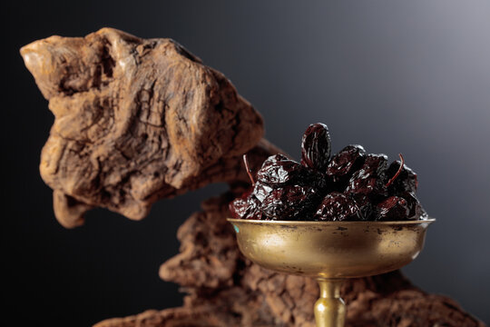 Spicy dried black olives in a vintage brass bowl on a background of weathered olive tree snags.