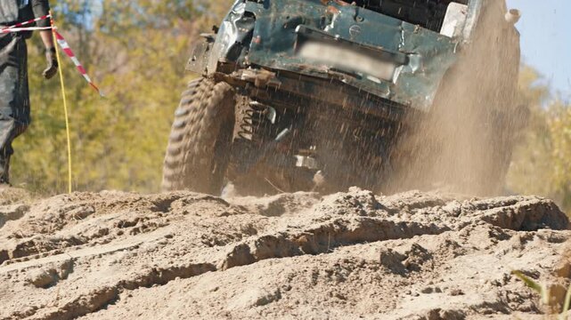 Action shot of modified car competing in off road race. Vehicle speeds up sandy hill, kicking up large cloud of dust and dirt. Bright daylight illuminates dynamic scene