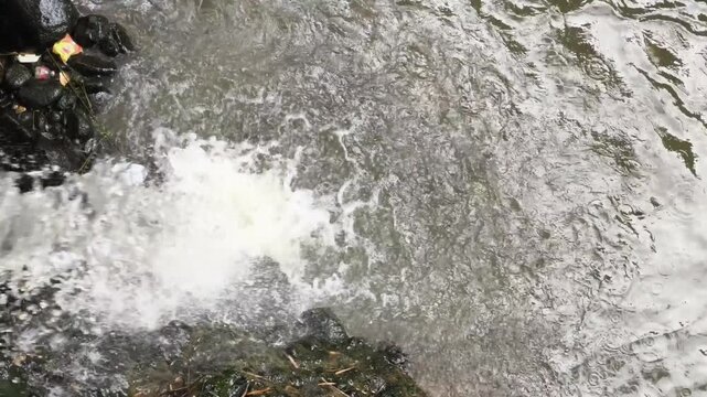 Rapid flow of white frothy river water flowing fast among natural river stones.
