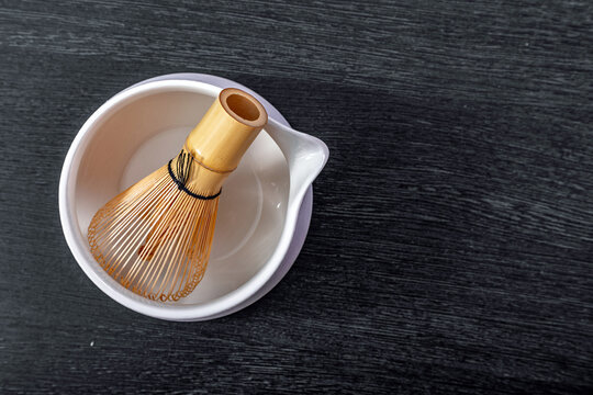 Bamboo matcha whisk inside ceramic tea bowl on dark wooden table. Japanese tea ceremony equipment for preparing traditional powdered green tea. Culinary tool for healthy lifestyle