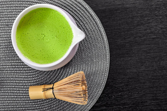 Green matcha tea in bowl with bamboo whisk. Traditional Japanese beverage for relaxation and healthy lifestyle. Organic drink on dark textured table for wellness and tea ceremony