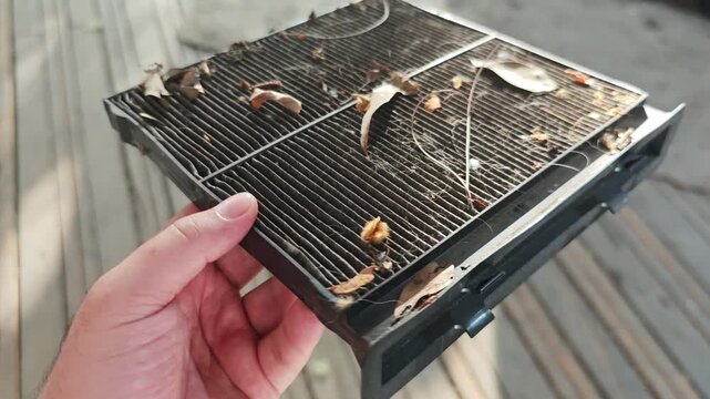 Service technician holding a clogged and dirty cabin air filter with leaves, dust, and debris. Regular car maintenance and repair service concept