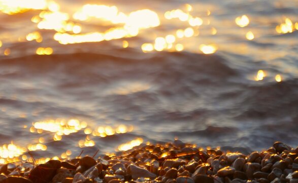Beach with glowing pebbles by the sea with waves splash in golden sunset, summer beach background
