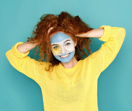 Portrait of happy woman with the flag of Argentina painted on her face. Football or soccer team fan, sport event, faceart and patriotism concept. Studio shot at blue background, copy space