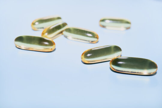 Fish oil capsules scattered on a light blue background, representing wellness and nutrition