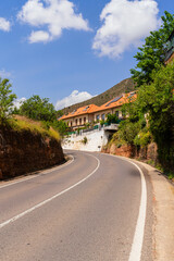 Naklejka premium Sundrenched curve of a quiet rural road leads through a hillside village, with terracottaroofed homes, lush greenery, and mountain backdrop evoking authentic slow travel in Mediterranean.