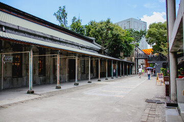 Naklejka premium TAIPEI, TAIWAN – FEBRUARY 15, 2022: Tourists walking on a pathway next to historical factory warehouse buildings and a rusty metal pavilion corridor at Huashan 1914 Creative Park.