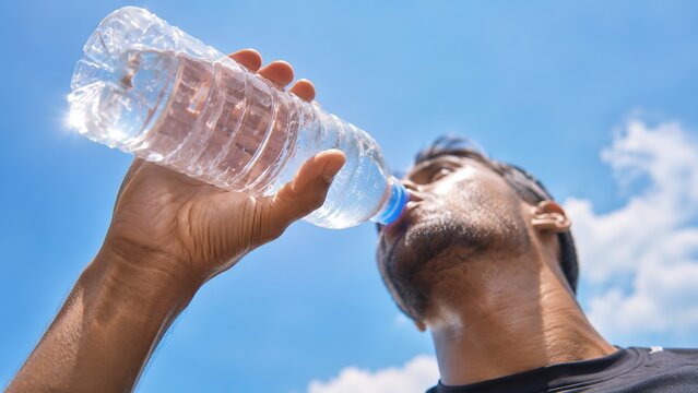 A man savoring a cool beverage from a water bottle beneath a clear blue sky highlighting the significance of staying hydrated and maintaining wellness while engaging in outdoor adventures