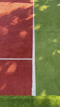 Modern tennis court with a combination playing surface under bright summer sunlight, featuring soft tree shadows and clean geometric lines. A perfect setting for active recreation, sports resorts
