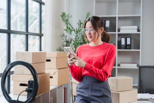 Young woman entrepreneur checking smartphone in packaging area with boxes