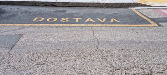 Fototapeta premium A yellow parking zone designated for delivery vehicles with the Croatian word DOSTAVA painted on the street asphalt.