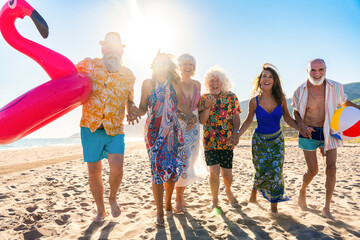 Obraz premium Happy group of senior friends bonding at the beach during summertime - Cheerful old and mature people having fun at the sea on summer vacation, elderly lifestyle concepts