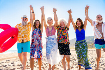 Obraz premium Happy group of senior friends bonding at the beach during summertime - Cheerful old and mature people having fun at the sea on summer vacation, elderly lifestyle concepts