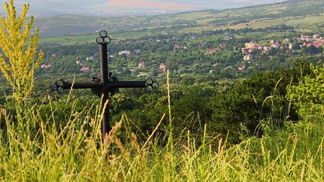 Black iron cross on the edge of a cliff with a panoramic view of Iasi city from the Bucium relay hill.