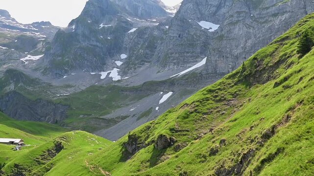 Rugged Swiss Alps with green slopes and lingering snowfields on a summer hike above Engelberg, Switzerland.