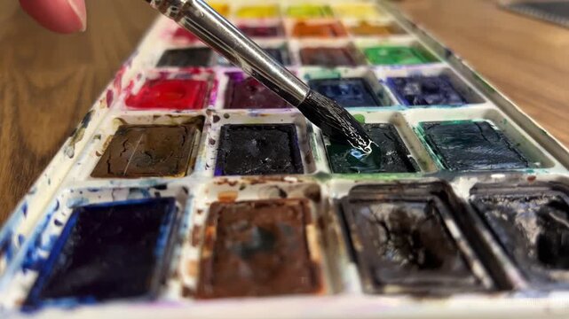 Watercolor paint set with brush picking up paint close up, watercolor painting
