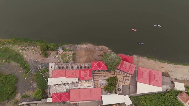 Surat, Gujarat / India - July 8 2026: Aerial drone view of a cremation ground on the riverbank with buildings, small boats and surrounding landscape in Surat, Gujarat, India.