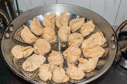 batch of healthy whole wheat raw momos arranged on a traditional perforated metal plate placed inside a kadhai for steaming in an Indian home kitchen. 