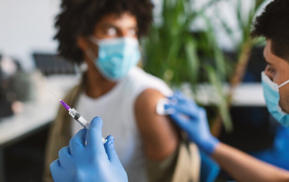 Clinical trial for new modern vaccine during global pandemic. Guy in medical face mask getting injection at hospital. Doctor preparing syringe to give a shot, rubbing arm with cotton pad