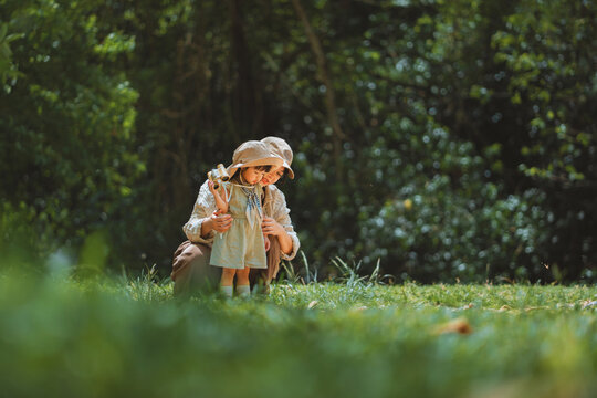 Happy Asian mother and her little daughter with binoculars exploring nature together in green park, cute toddler child learning outdoors on family summer vacation for early childhood education, parent