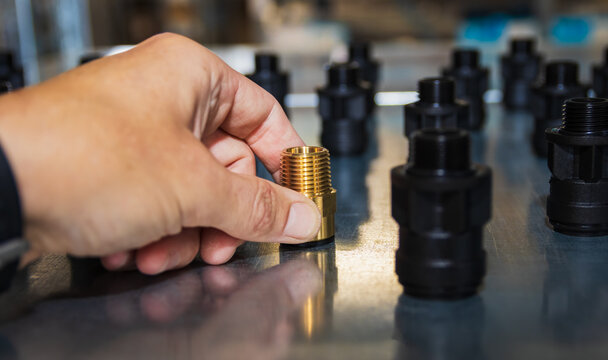 Close-up view of a hand placing a brass threaded pipe fitting among black plastic connectors on a metal surface